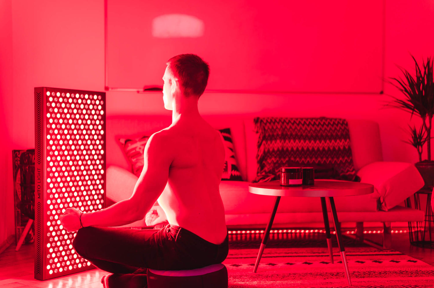 Man zit voor een Rood Licht Therapie paneel in zijn woonkamer